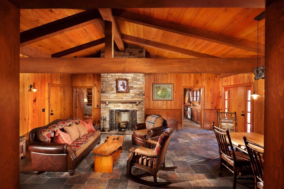 На фото: большая открытая гостиная комната в стиле рустика с коричневыми стенами, полом из сланца, стандартным камином и фасадом камина из камня
