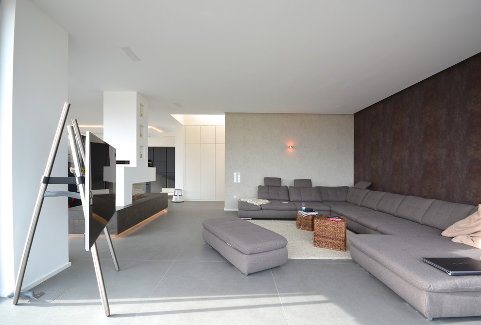 Ejemplo de sala de estar abierta moderna con chimenea de doble cara, marco de chimenea de yeso, televisor independiente, suelo gris y paredes marrones