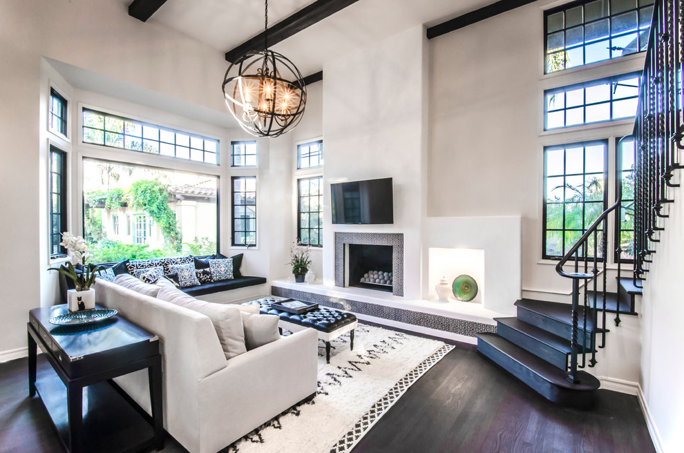 Expansive mediterranean open plan games room in Santa Barbara with white walls, dark hardwood flooring, a standard fireplace, a tiled fireplace surround and a wall mounted tv.