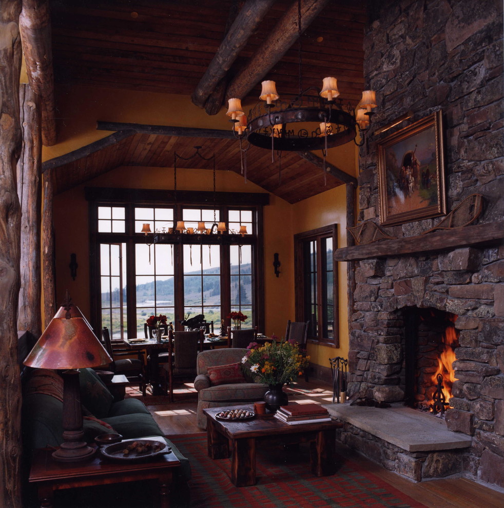 Modelo de sala de estar abierta rústica con suelo de madera en tonos medios, todas las chimeneas y marco de chimenea de piedra