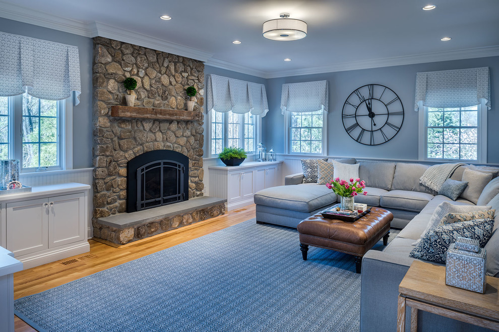 Идея дизайна: большая изолированная гостиная комната в стиле неоклассика (современная классика) с синими стенами, паркетным полом среднего тона, стандартным камином, фасадом камина из камня и телевизором на стене