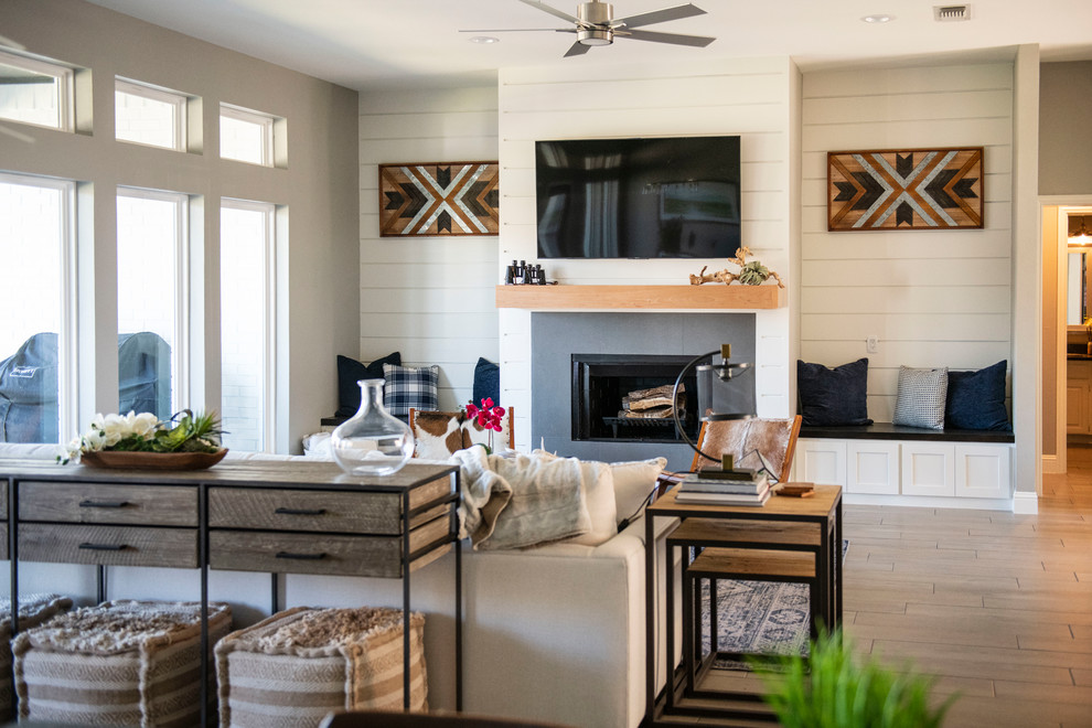 Medium sized farmhouse open plan games room in Dallas with white walls, porcelain flooring, a standard fireplace, a wooden fireplace surround, a wall mounted tv and grey floors.
