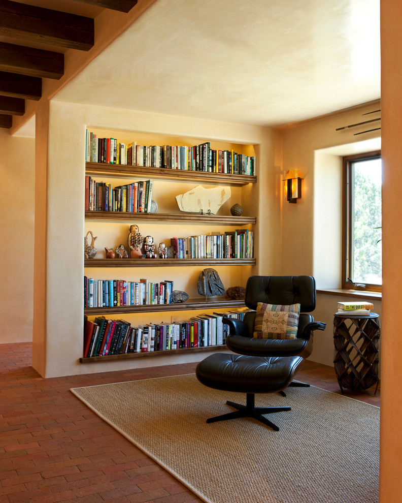 Imagen de sala de estar con biblioteca mediterránea con paredes beige y suelo de ladrillo