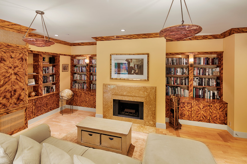 Diseño de sala de estar con biblioteca cerrada mediterránea de tamaño medio con paredes amarillas, suelo de madera clara, todas las chimeneas y marco de chimenea de piedra