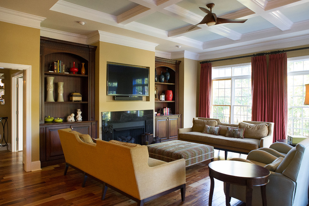Imagen de sala de estar abierta actual grande con paredes amarillas, suelo de madera en tonos medios, todas las chimeneas, marco de chimenea de piedra y televisor colgado en la pared