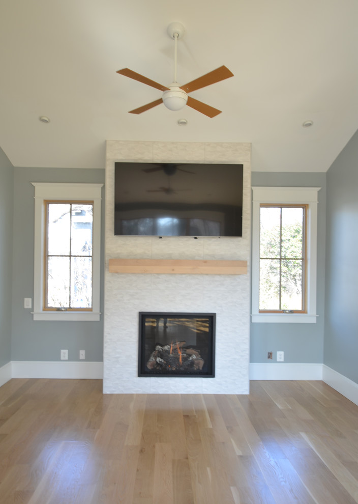 Photo of a medium sized contemporary open plan games room in DC Metro with blue walls, light hardwood flooring, a standard fireplace, a tiled fireplace surround, a wall mounted tv and brown floors.