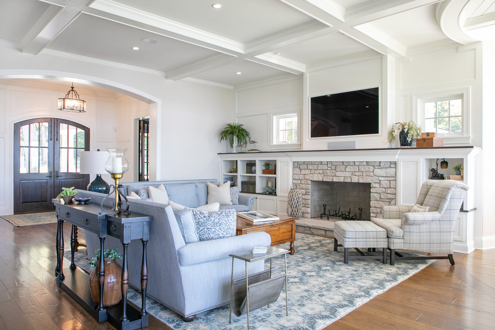 Пример оригинального дизайна: большая гостиная комната в морском стиле с белыми стенами, стандартным камином, фасадом камина из камня, паркетным полом среднего тона, телевизором на стене, синим диваном и ковром на полу
