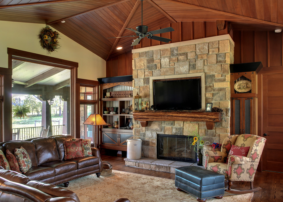 Diseño de sala de estar de estilo de casa de campo con paredes beige, suelo de madera oscura, todas las chimeneas, marco de chimenea de piedra y televisor colgado en la pared