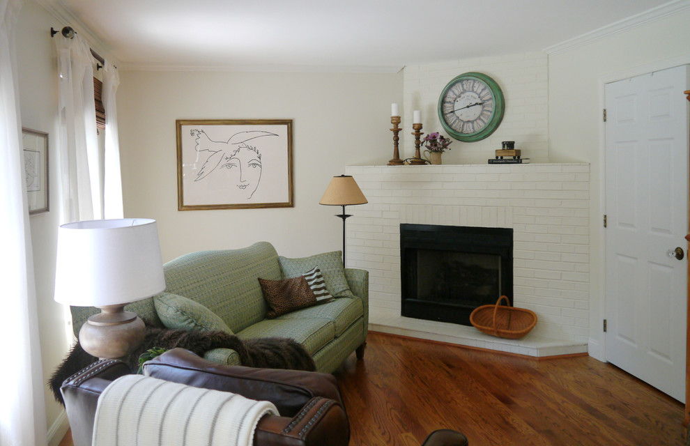Exemple d'une petite salle de séjour nature ouverte avec un mur beige, un sol en bois brun, une cheminée d'angle, un manteau de cheminée en brique et un téléviseur dissimulé.