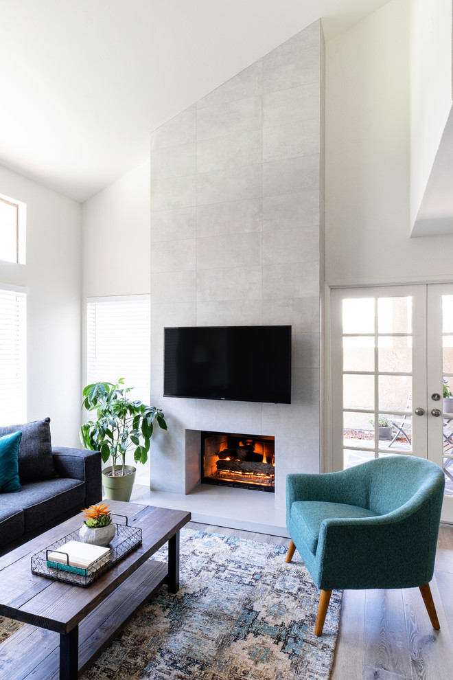 Cette photo montre une grande salle de séjour moderne ouverte avec un mur blanc, sol en stratifié, une cheminée standard, un manteau de cheminée en carrelage, un téléviseur fixé au mur et un sol gris.