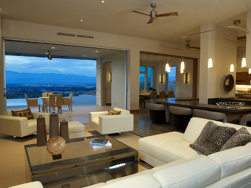 На фото: открытая гостиная комната в стиле модернизм с бежевыми стенами, бетонным полом и телевизором на стене без камина