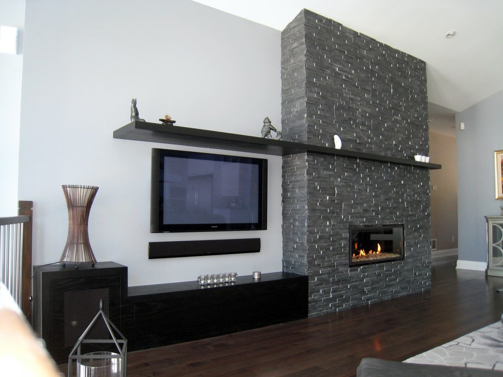 This is an example of a medium sized modern open plan games room in Toronto with dark hardwood flooring, a standard fireplace, a stone fireplace surround, a built-in media unit and grey walls.