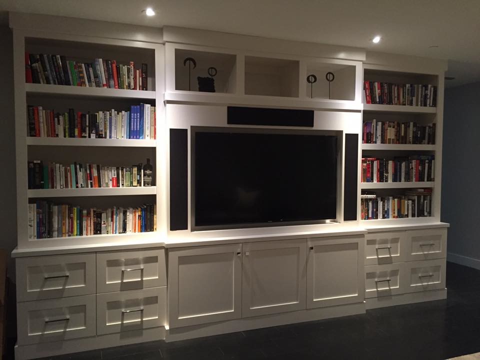 Imagen de sala de estar con biblioteca cerrada clásica renovada de tamaño medio sin chimenea con paredes blancas, suelo de madera oscura, pared multimedia y suelo negro