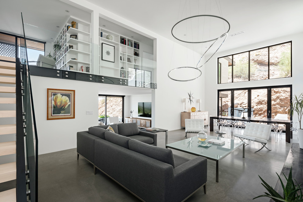 На фото: двухуровневая гостиная комната в стиле модернизм с белыми стенами, бетонным полом, стандартным камином, фасадом камина из штукатурки и серым полом