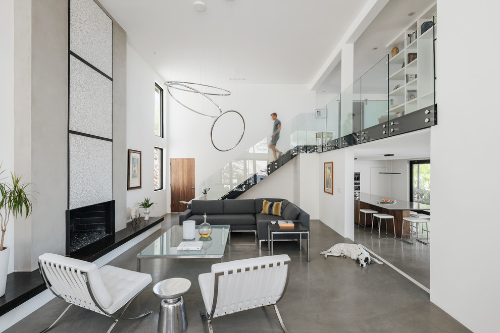 Источник вдохновения для домашнего уюта: двухуровневая гостиная комната в стиле модернизм с белыми стенами, бетонным полом, стандартным камином, фасадом камина из штукатурки и серым полом