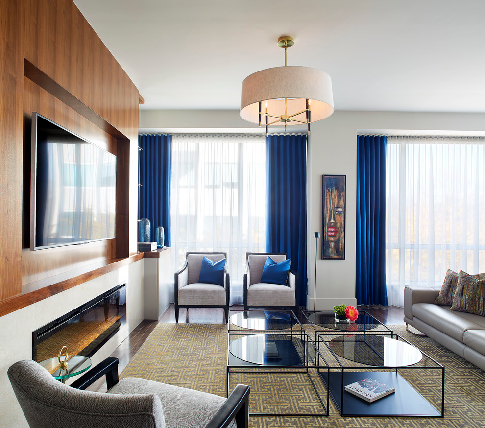 На фото: гостиная комната в стиле неоклассика (современная классика) с белыми стенами, темным паркетным полом, горизонтальным камином, телевизором на стене и синими шторами