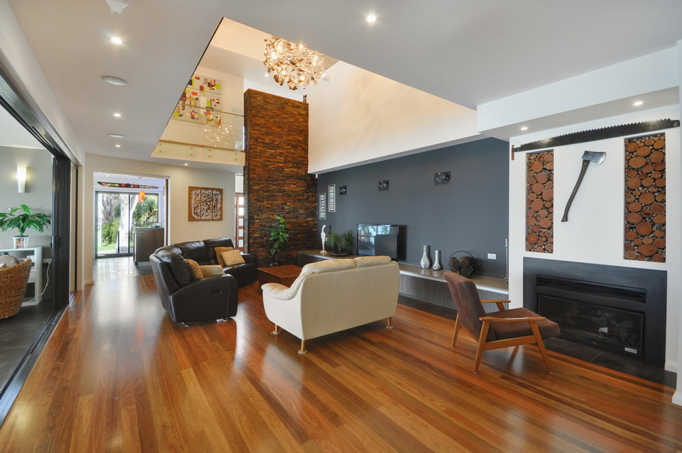 Aménagement d'une grande salle de séjour moderne ouverte avec un mur multicolore, un sol en bois brun, une cheminée standard, un manteau de cheminée en plâtre et un téléviseur indépendant.