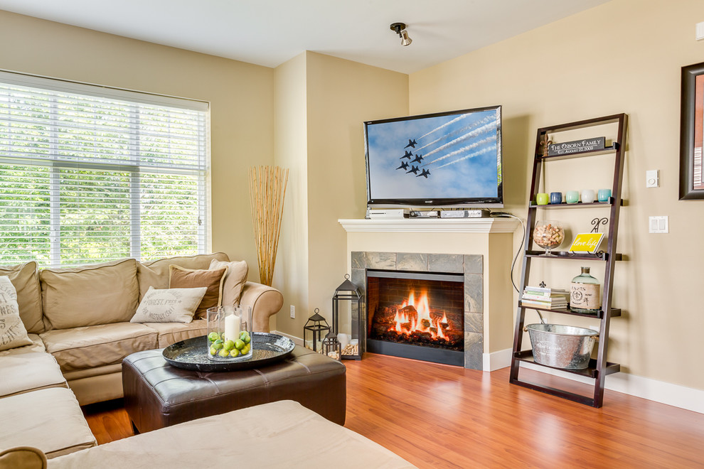 Foto de sala de estar tradicional con paredes beige, suelo de madera en tonos medios, chimenea de esquina, marco de chimenea de baldosas y/o azulejos y televisor en una esquina