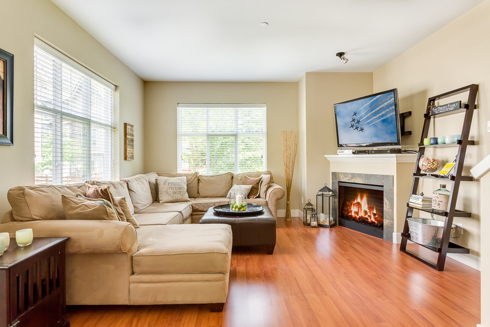 Cette image montre une salle de séjour traditionnelle avec un mur beige, un sol en bois brun, une cheminée d'angle, un manteau de cheminée en carrelage et un téléviseur d'angle.
