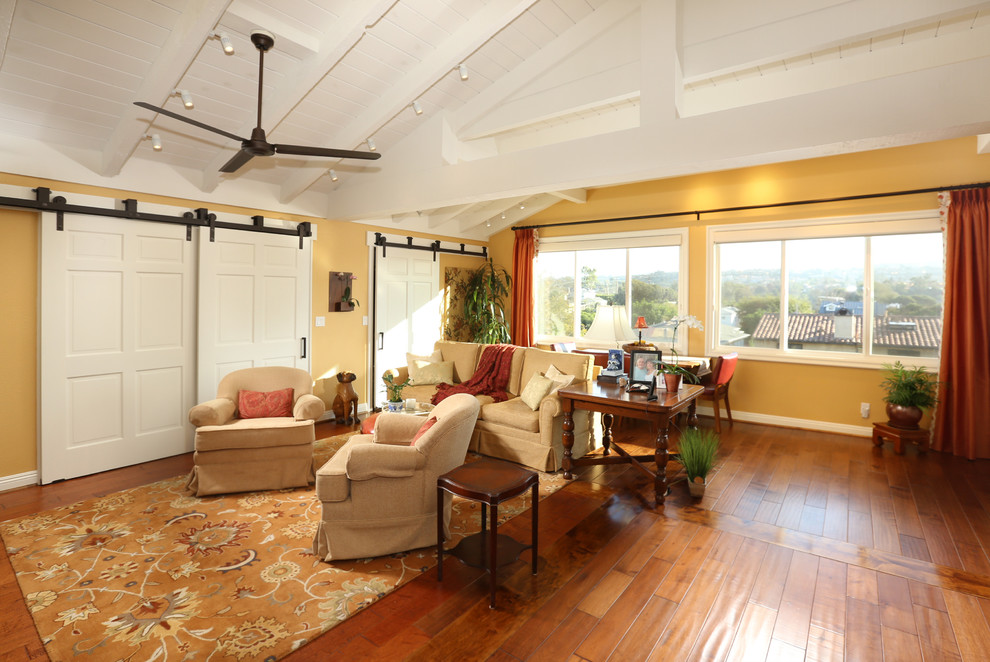Mittelgroßes, Offenes Klassisches Wohnzimmer ohne Kamin mit gelber Wandfarbe, braunem Holzboden, TV-Wand und braunem Boden in Los Angeles