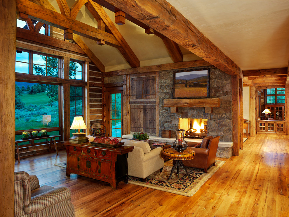 Cette photo montre une très grande salle de séjour montagne ouverte avec un mur beige, un sol en bois brun, une cheminée standard, un manteau de cheminée en pierre et éclairage.