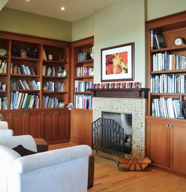 Foto di un soggiorno tradizionale di medie dimensioni con libreria, pareti grigie, pavimento in legno massello medio, camino classico e cornice del camino piastrellata