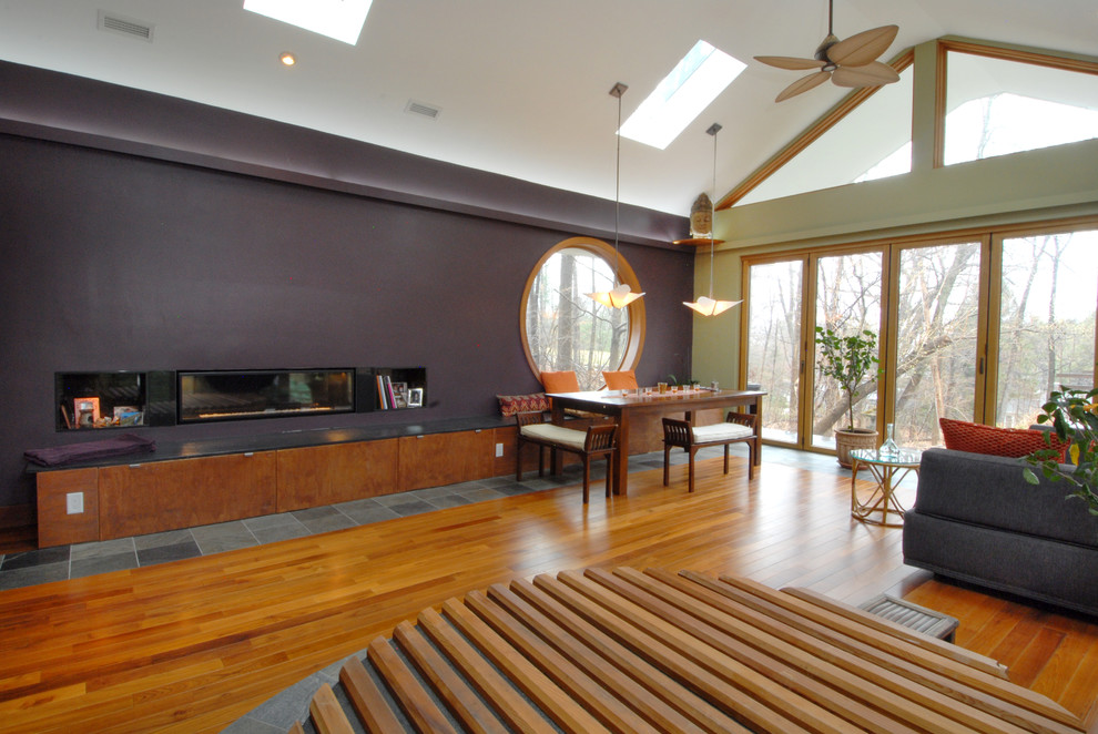 Modelo de sala de estar cerrada ecléctica grande sin televisor con paredes púrpuras, suelo de madera en tonos medios y chimenea lineal
