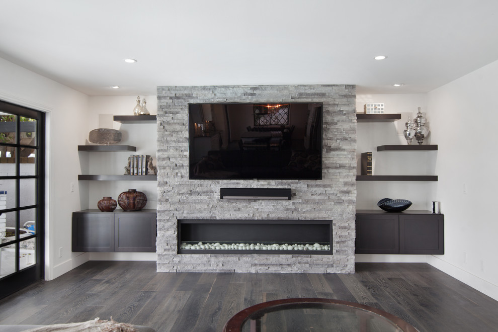 Imagen de sala de juegos en casa abierta moderna de tamaño medio con paredes grises, suelo de madera oscura, chimeneas suspendidas, marco de chimenea de piedra y pared multimedia