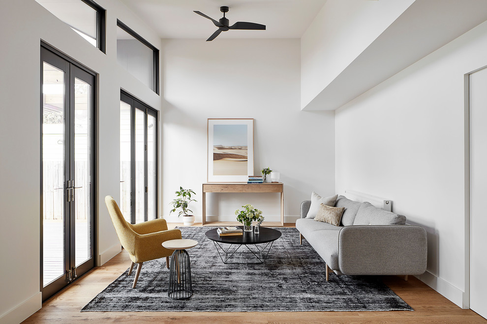 Imagen de sala de estar abierta, abovedada y blanca actual de tamaño medio con paredes blancas, suelo de madera clara, pared multimedia y suelo marrón