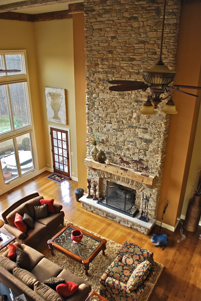 Ejemplo de sala de estar abierta tradicional grande con paredes beige, suelo de madera clara, marco de chimenea de piedra, todas las chimeneas y televisor retractable