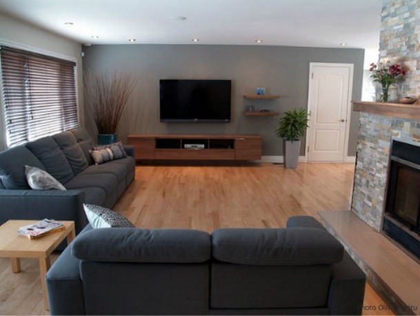 Cette image montre une grande salle de séjour design ouverte avec un mur gris, parquet clair, une cheminée standard, un manteau de cheminée en pierre et un téléviseur fixé au mur.