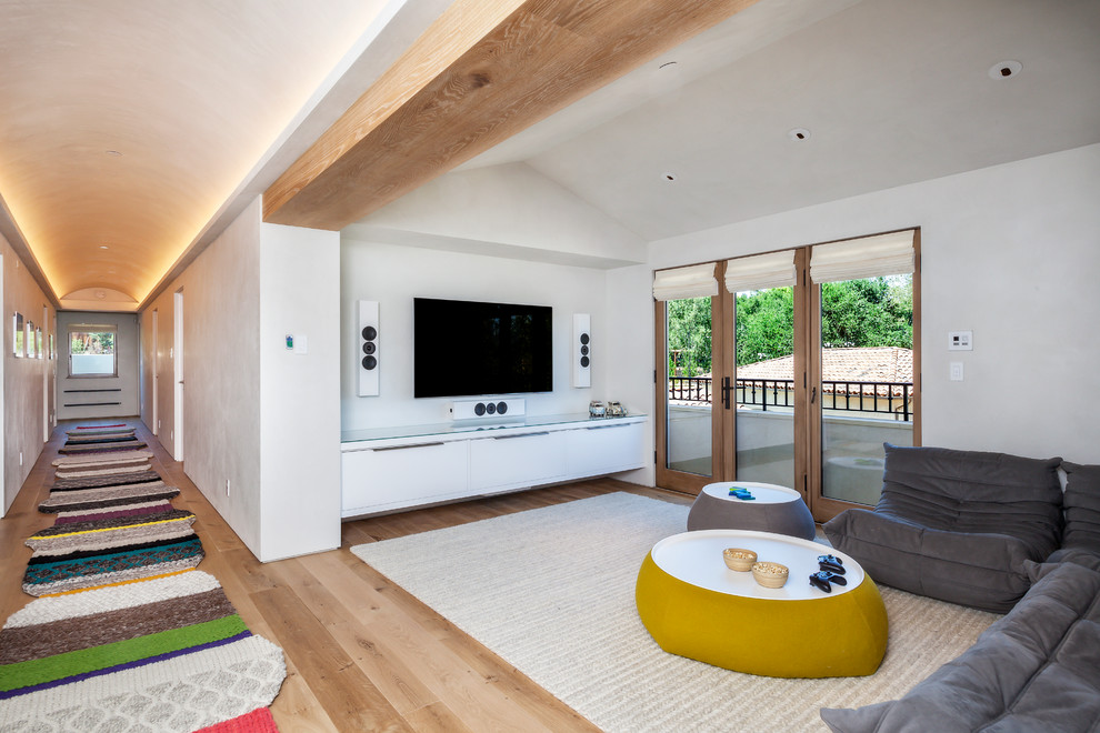 Стильный дизайн: гостиная комната в современном стиле с белыми стенами, паркетным полом среднего тона и телевизором на стене - последний тренд