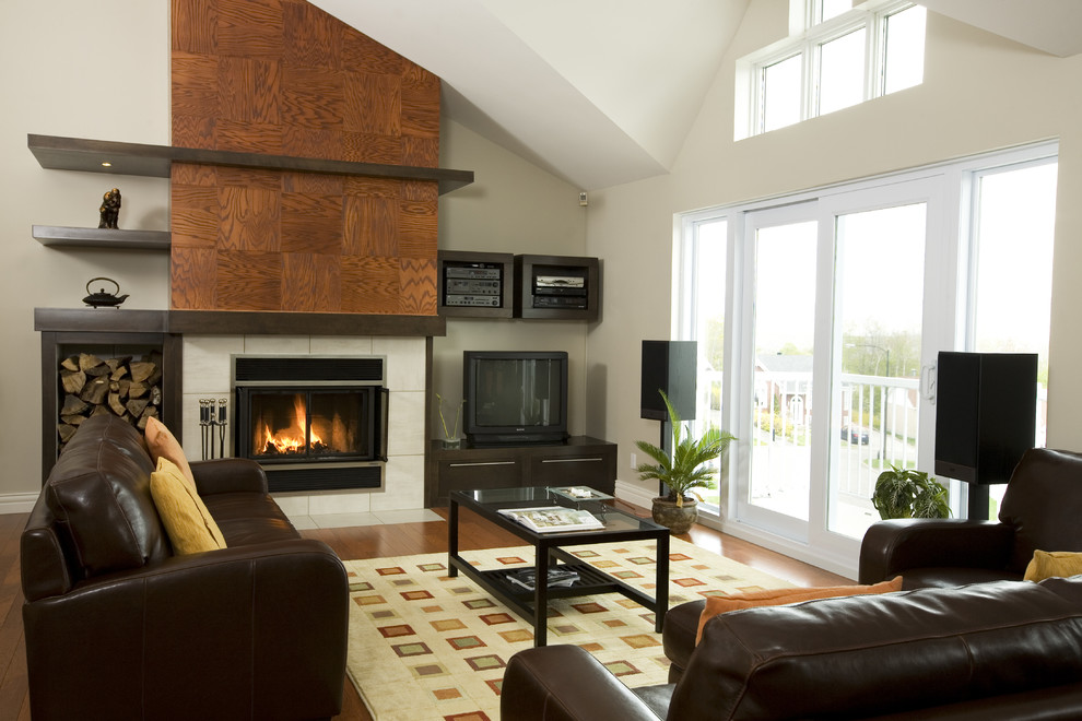 Photo of a medium sized modern open plan games room in Montreal with grey walls, medium hardwood flooring, a standard fireplace, a tiled fireplace surround, a freestanding tv and brown floors.