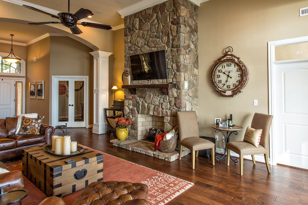 Cette image montre une grande salle de séjour chalet ouverte avec un mur marron, un sol en bois brun, une cheminée standard, un manteau de cheminée en pierre et un téléviseur fixé au mur.