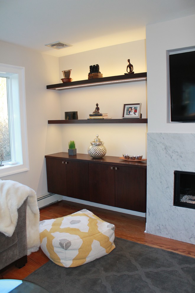 Modelo de sala de estar abierta moderna de tamaño medio con paredes grises, suelo de madera en tonos medios, chimenea lineal, marco de chimenea de piedra y pared multimedia