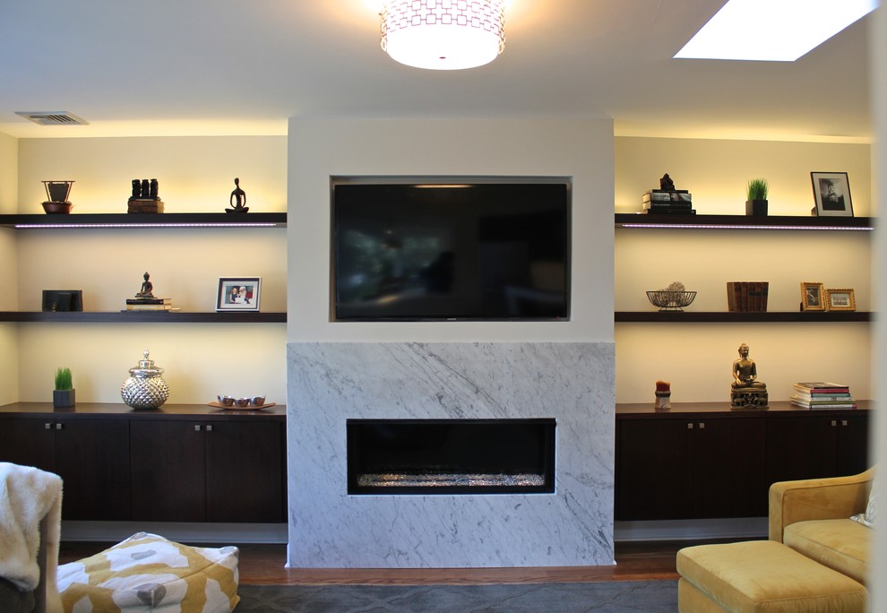 Ejemplo de sala de estar abierta minimalista de tamaño medio con paredes grises, suelo de madera en tonos medios, chimenea lineal, marco de chimenea de piedra y pared multimedia