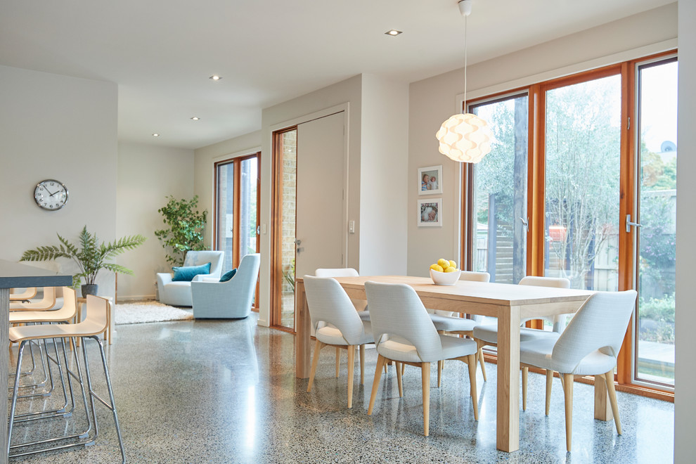 Modelo de sala de estar abierta nórdica de tamaño medio sin chimenea con paredes blancas, suelo de cemento, televisor colgado en la pared y suelo gris