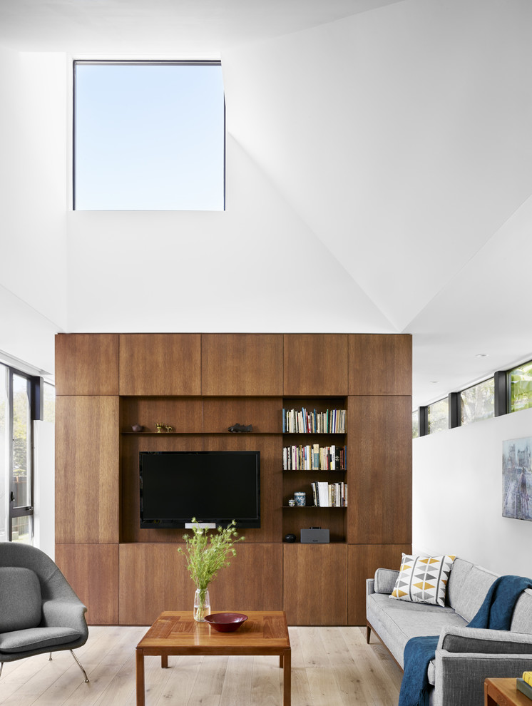 Foto de sala de estar con biblioteca abierta contemporánea sin chimenea con paredes blancas, suelo de madera clara y pared multimedia