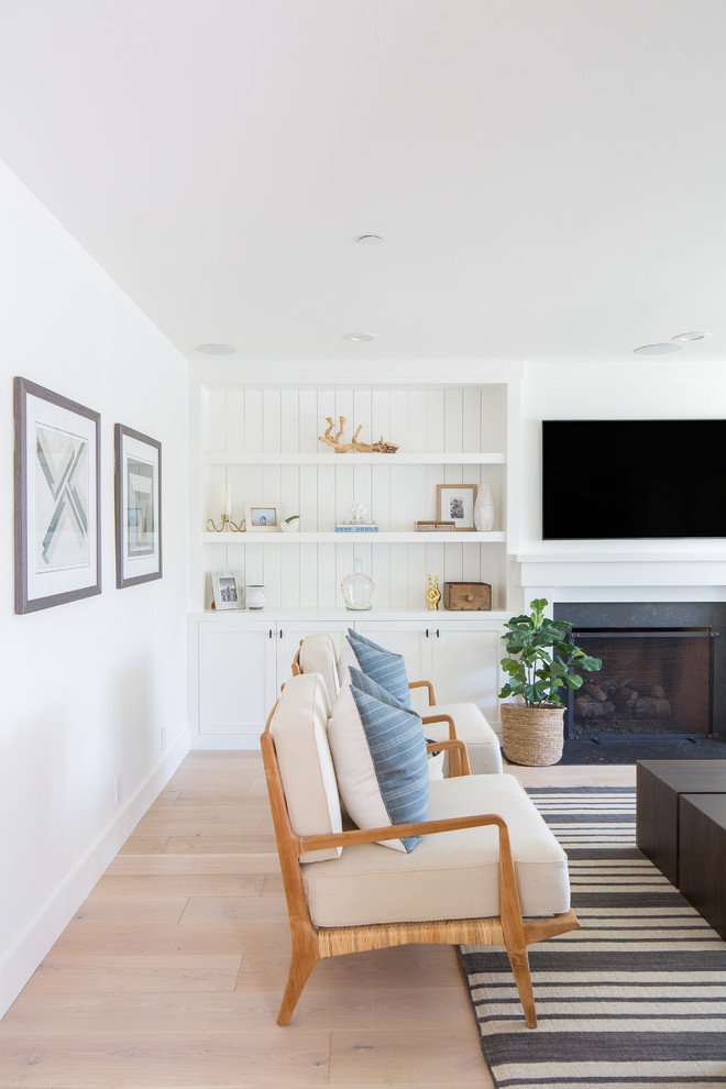 Abgetrenntes Maritimes Wohnzimmer mit weißer Wandfarbe, hellem Holzboden, Kamin, Kaminumrandung aus Stein, Multimediawand und weißem Boden in Orange County