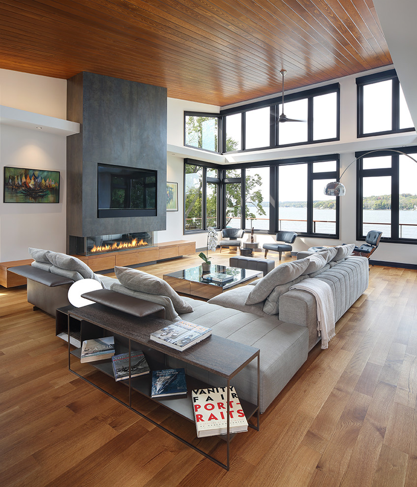 Ejemplo de sala de estar abierta actual con paredes blancas, suelo de madera en tonos medios, chimenea lineal y televisor colgado en la pared