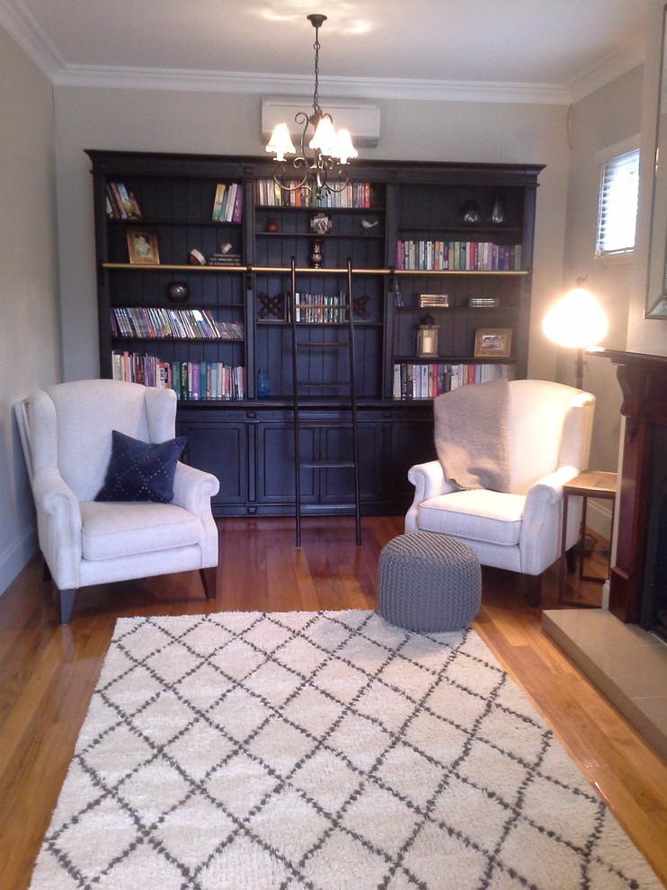 Esempio di un piccolo soggiorno chic aperto con libreria, pareti beige, parquet chiaro, camino classico, cornice del camino in legno e nessuna TV