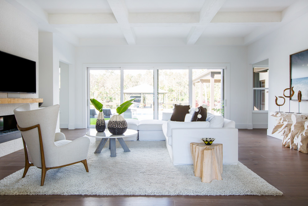 Modelo de sala de estar cerrada costera con paredes blancas, suelo de madera oscura, televisor colgado en la pared y suelo marrón