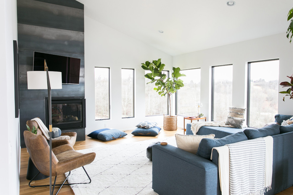 На фото: гостиная комната среднего размера в современном стиле с белыми стенами, угловым камином, фасадом камина из металла, телевизором на стене, паркетным полом среднего тона, коричневым полом и синим диваном с