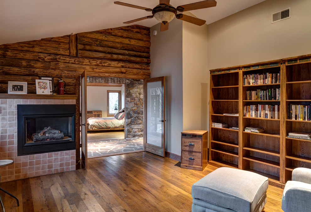 Aménagement d'une grande salle de séjour montagne fermée avec une bibliothèque ou un coin lecture, un mur beige, parquet clair, cheminée suspendue, un manteau de cheminée en brique et un sol marron.