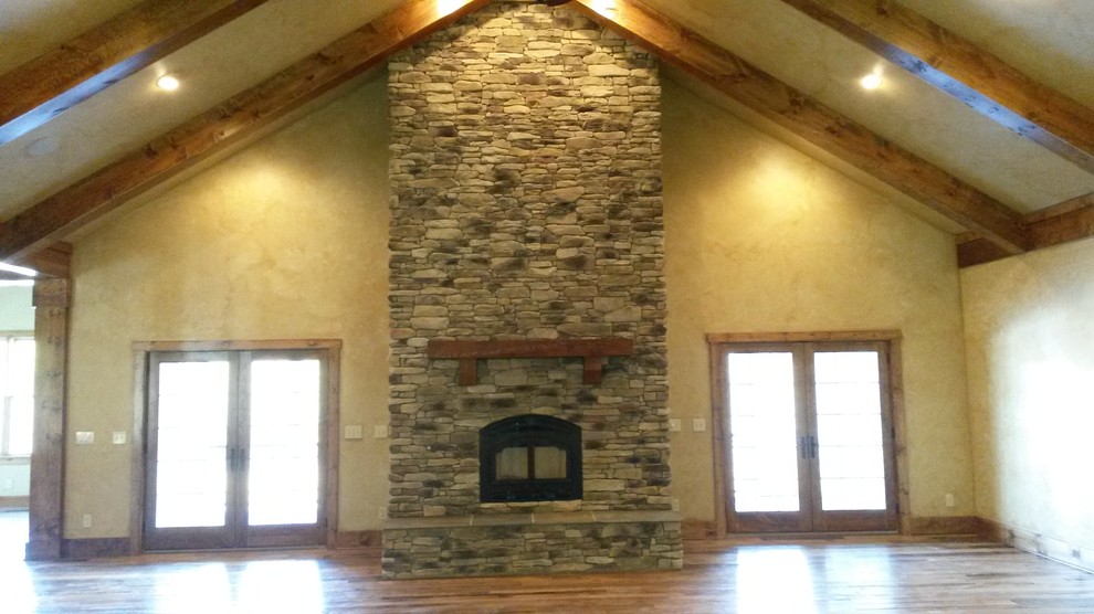 Imagen de sala de estar abierta rural con suelo de madera en tonos medios, estufa de leña y marco de chimenea de piedra