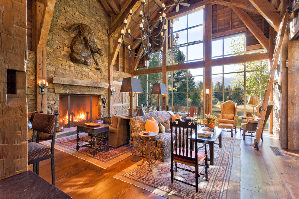 Imagen de sala de estar abierta rural con suelo de madera en tonos medios, todas las chimeneas, marco de chimenea de piedra y alfombra