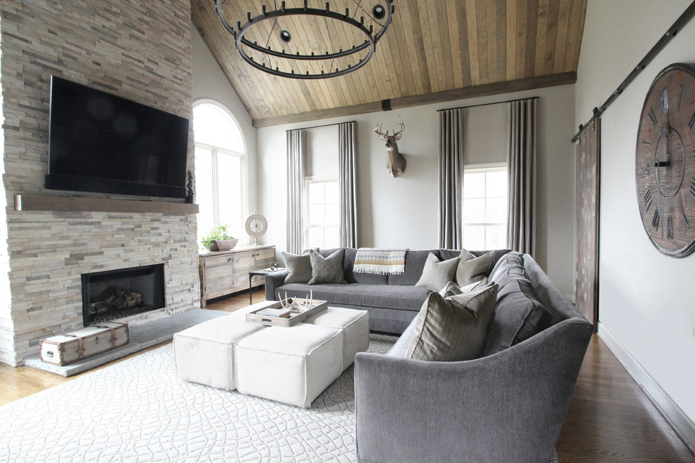 Foto de sala de estar clásica renovada grande con paredes beige, suelo de madera en tonos medios, todas las chimeneas, marco de chimenea de piedra y televisor colgado en la pared