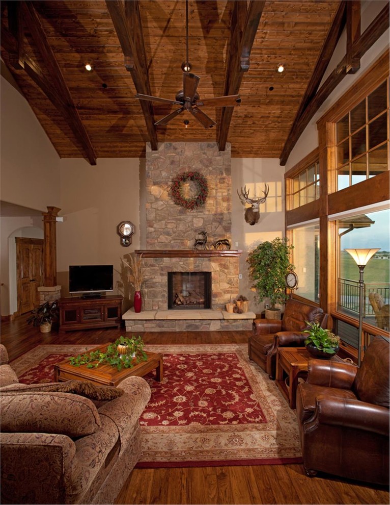 Cette photo montre une très grande salle de séjour montagne ouverte avec un mur beige, un sol en bois brun, une cheminée standard, un manteau de cheminée en pierre et un téléviseur indépendant.