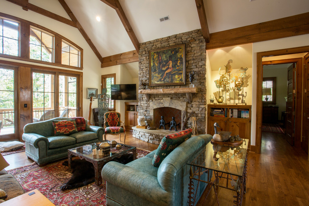 Example of a large arts and crafts open concept medium tone wood floor family room design in Other with beige walls, a standard fireplace, a stone fireplace and a wall-mounted tv