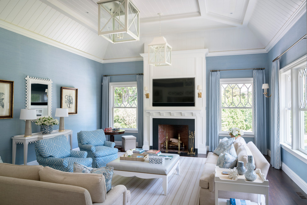 Cette image montre une grande salle de séjour marine ouverte avec un mur bleu, parquet foncé, une cheminée standard, un manteau de cheminée en pierre, un téléviseur fixé au mur et un sol marron.